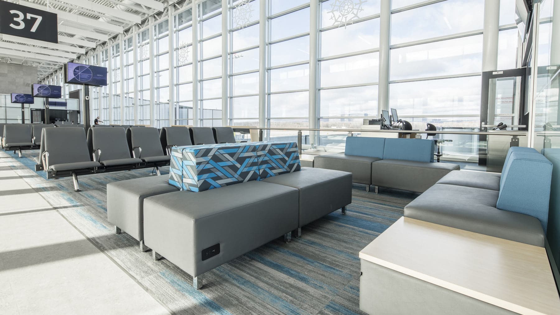 Modern airport gate area with modular lounge seating, integrated power outlets, and floor-to-ceiling windows overlooking the tarmac