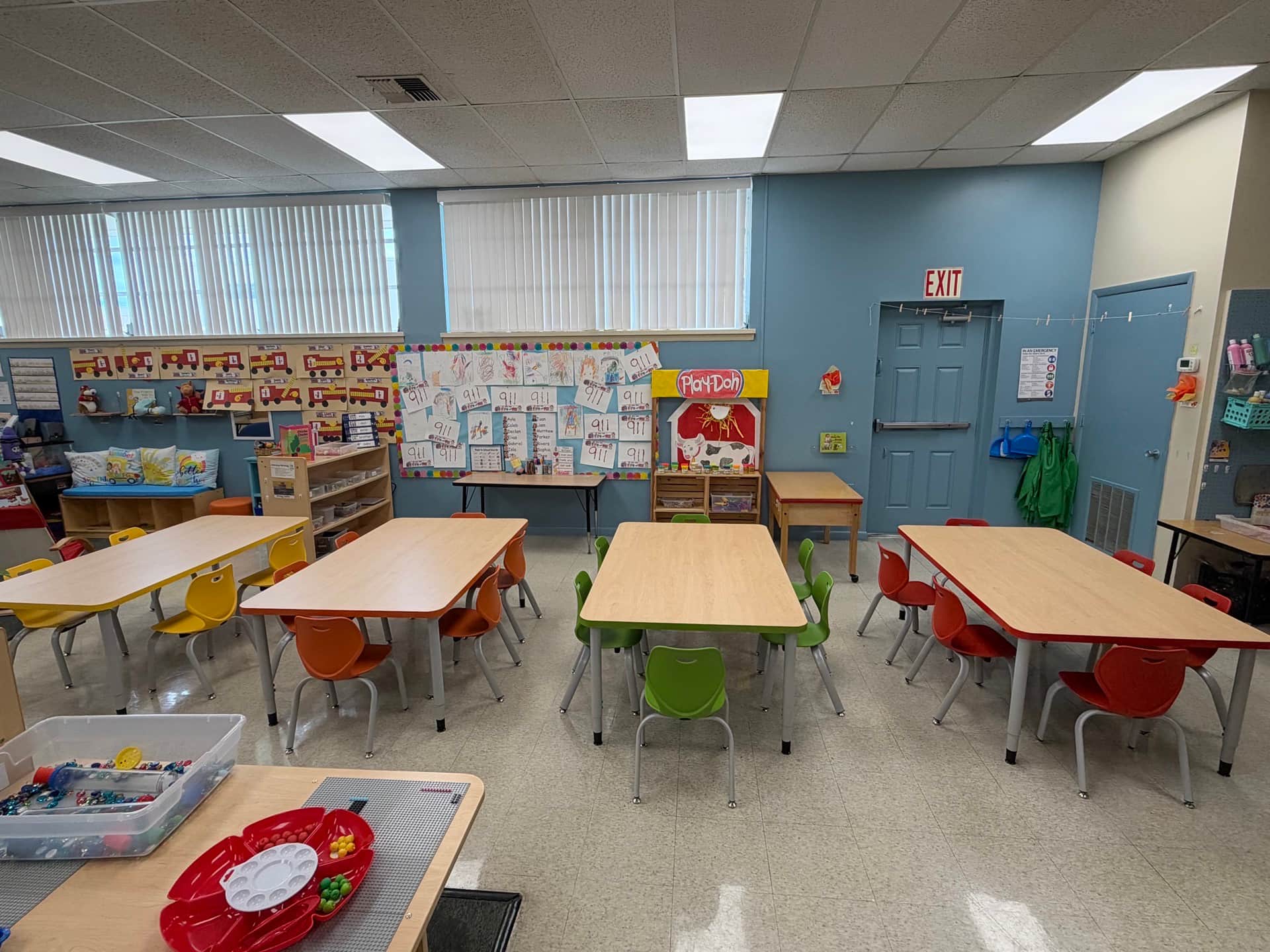 Elementary classroom with wood-tone trapezoid tables and color-coded stack chairs in yellow, orange, green, and red