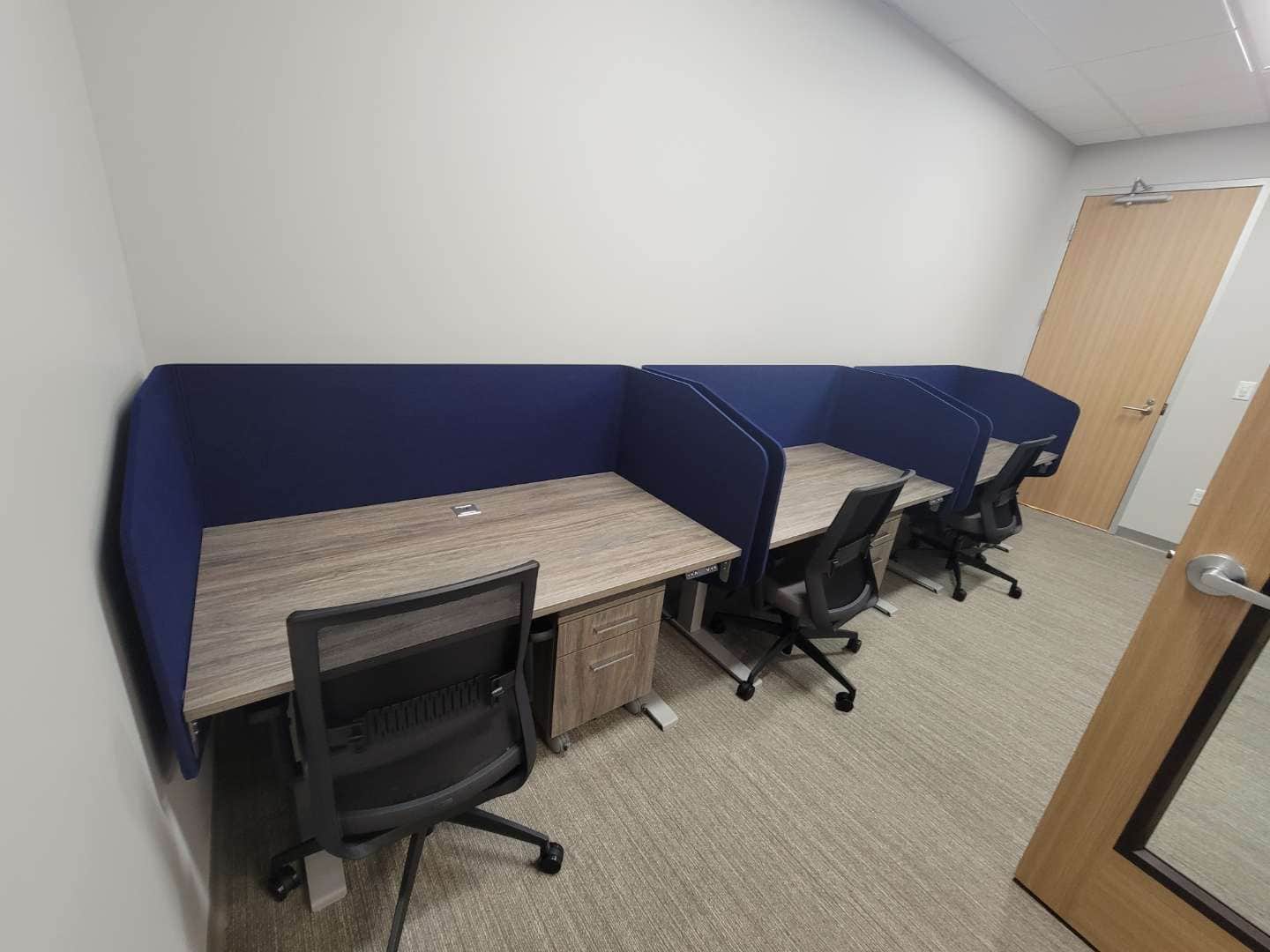 Three bench-style desks with navy privacy screens and task chairs along a wall