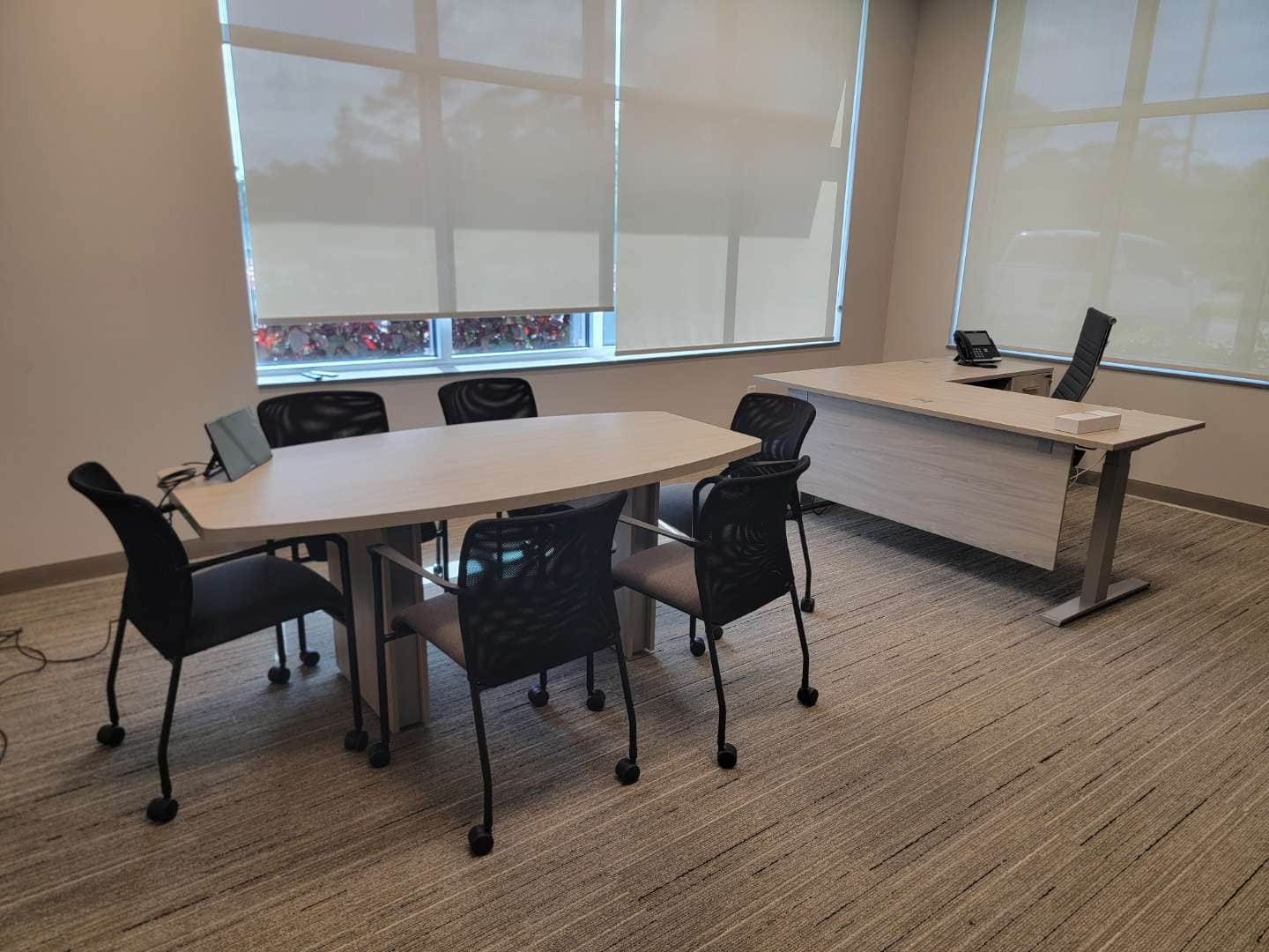 Private office with a small oval conference table and five chairs alongside an L-shaped desk