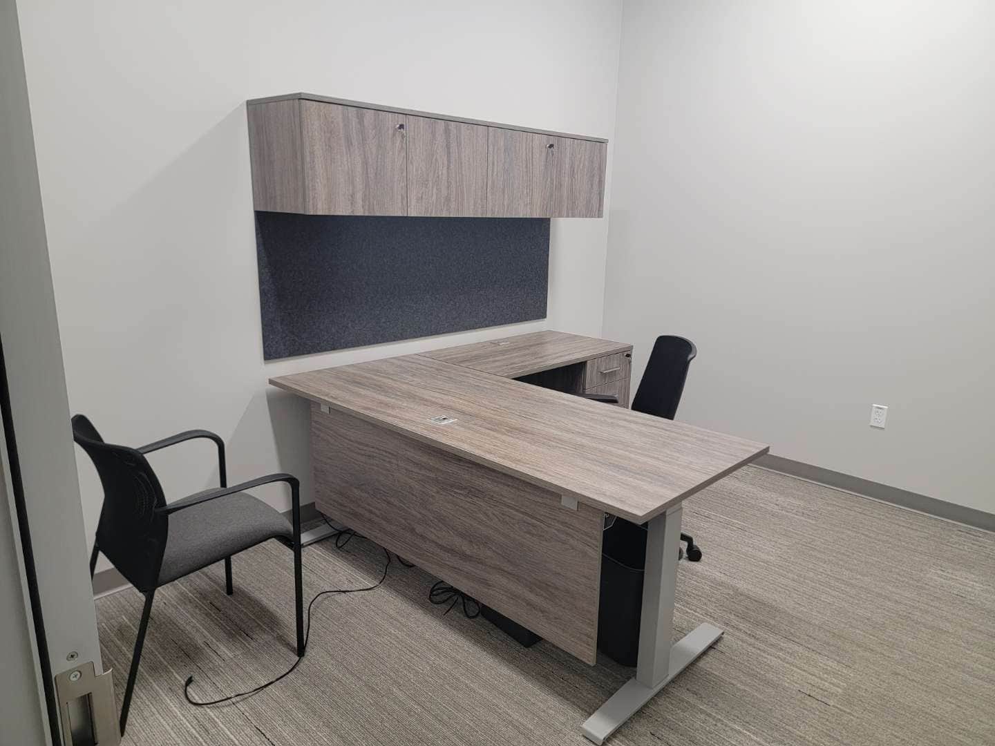Private office with an L-shaped desk, overhead storage hutch, and two guest chairs