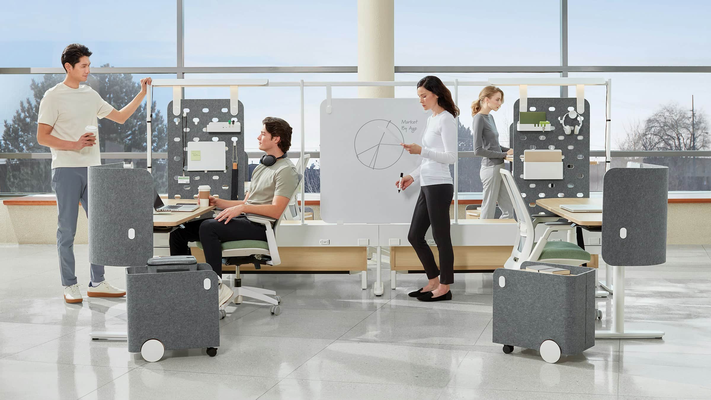 Team working at height-adjustable workstations with acoustic screens in a bright, window-lined office