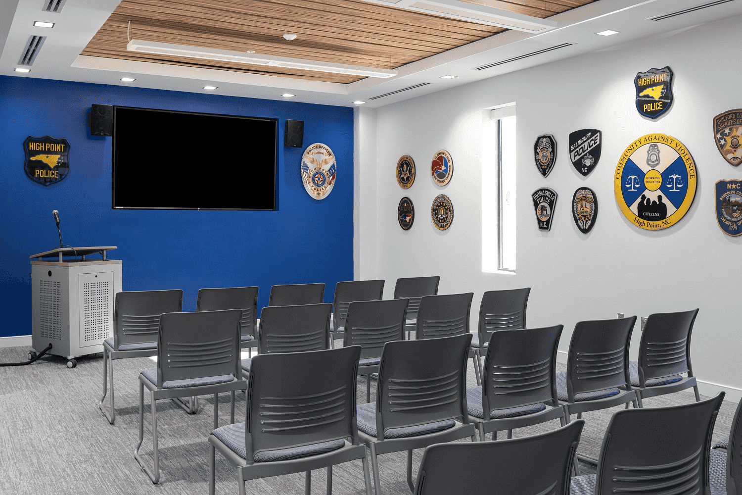 Police department briefing and training room with rows of stack chairs, a lectern, and agency patches on the wall