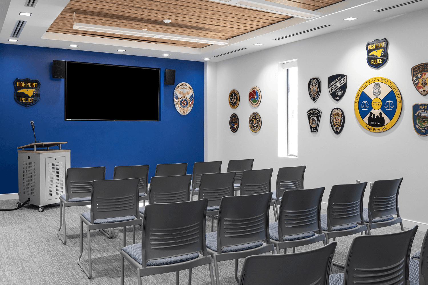 Police department briefing and training room with rows of stack chairs, a lectern, and agency patches on the wall